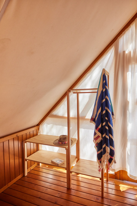 Sonnenlicht fällt in eine gemütliche Ecke des Glamping Tipi Retama mit Holzregal und buntem Handtuch.