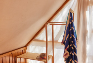 Sonnenlicht fällt in eine gemütliche Ecke des Glamping Tipi Retama mit Holzregal und buntem Handtuch.