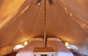 Indvendigt billede af Glamping Bell Marisma teepee telt med to opredte senge og hyggelige lamper.