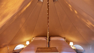 Innenansicht des Glamping Bell Marisma Tipi-Zeltes mit zwei Betten und stimmungsvoller Beleuchtung.