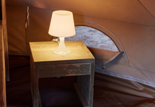Interior de la tienda Glamping Bell Marisma en TAIGA Conil, España, con mesa de noche y lámpara encendida.