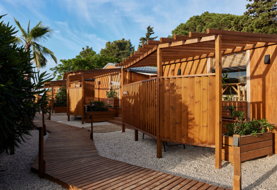 Vista exterior de cabañas de madera en Bungalow Premium Levante con terrazas, plantas y cielo azul despejado.