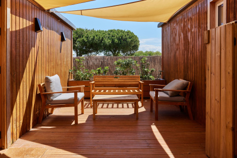 Buitenterras met houten zetels en zonnedoek aan Bungalow Premium Levante, TAIGA Conil, Spanje.