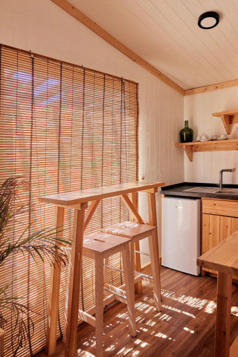 Zonnig houten bungalowinterieur met bamboe jaloezieën, hoge tafel en krukken bij TAIGA Conil, Spanje.