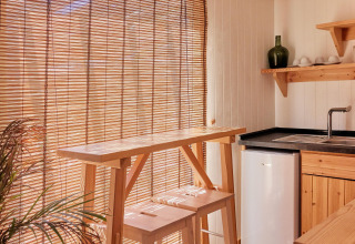 Intérieur lumineux d’un bungalow en bois avec stores en bambou, bar et tabourets à TAIGA Conil, Espagne.