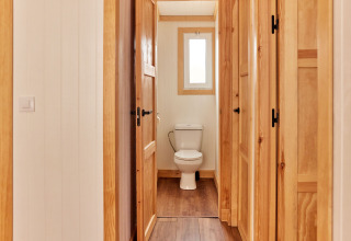 Vista interior de un baño con paneles de madera y un inodoro en Bungalow Premium Levante, TAIGA Conil, España.