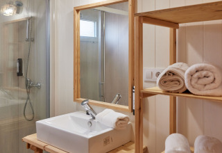 Baño moderno en Bungalow Premium Levante de TAIGA Conil, con ducha, lavabo y toallas enrolladas.
