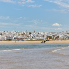 Vista de la playa y el mar cerca de Conil de la Frontera, Andalucía, España, con casas blancas al fondo.