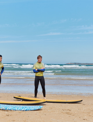 Instructor de surf enseñando técnicas básicas a tres alumnos en la playa cerca de Conil de la Frontera, España.