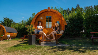 Dos personas relajándose frente a una cabaña con forma de barril en Tractor cabin en Biggesee, Alemania.