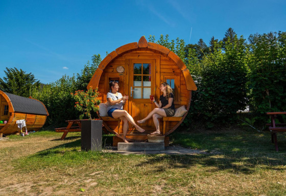 Dos personas relajándose frente a una cabaña con forma de barril en Tractor cabin en Biggesee, Alemania.