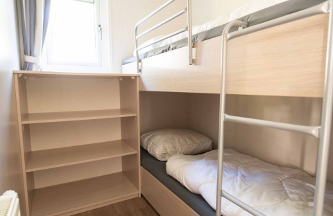 Vista de un dormitorio compacto con literas y estantería en Easy chalet, Eurocamping Vessem, Países Bajos.