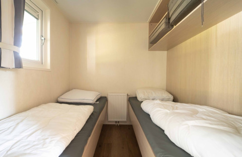 Dos camas individuales en una habitación luminosa del Easy chalet, Eurocamping Vessem BV, Países Bajos, con ventana.