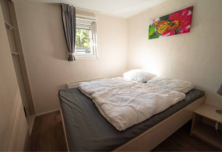 Schlafzimmer mit Doppelbett, weißer Bettdecke, Fenster, Schmetterlingsbild und Nachttisch im Easy chalet bei Eurocamping Vessem BV, Niederlande.