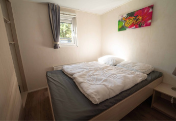 Schlafzimmer mit Doppelbett, weißer Bettdecke, Fenster, Schmetterlingsbild und Nachttisch im Easy chalet bei Eurocamping Vessem BV, Niederlande.
