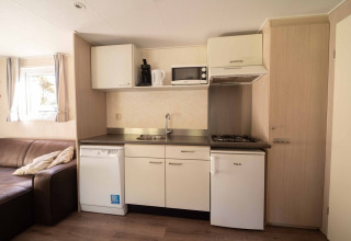 Kompakte Küchenzeile im Easy Chalet bei Eurocamping Vessem BV, Niederlande, mit Sofa und Geräten.