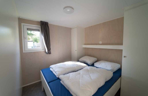 Dormitorio con dos camas individuales, sábanas azules y edredones blancos en una Woodlodge XL de Eurocamping Vessem BV.