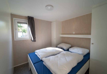 Dormitorio con dos camas individuales, sábanas azules y edredones blancos en una Woodlodge XL de Eurocamping Vessem BV.