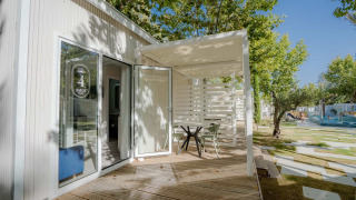 Buitenterras van Amos Studio lodge met tafel, stoelen, houten vloer en groen in een zonnige omgeving.