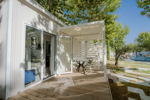 Buitenterras van Amos Studio lodge met tafel, stoelen, houten vloer en groen in een zonnige omgeving.