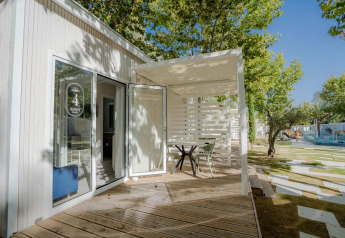 Terrasse extérieure du lodge Amos Studio avec table, chaises, parquet en bois et arbres par temps ensoleillé.