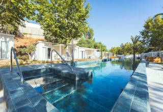 Piscina y spa en Amos Studio, Camping Costa del Sol Glamping Village, rodeados de cabañas y árboles.