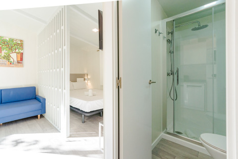 Amos Studio en Camping Costa del Sol Glamping Village en España con ducha, cama, sofá azul y decoración moderna.