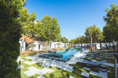 Area piscina moderna all'aperto con lettini, prati verdi e alberi in un assolato glamping spagnolo.