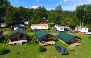 Foto de un camping con tiendas safari, caravanas y mucho césped verde, rodeado de árboles y naturaleza.