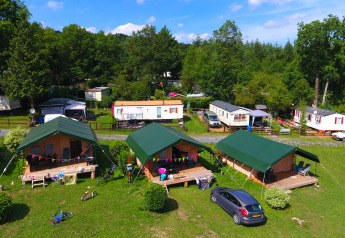 Billede af en campingplads med safaritelte, campingvogne og grønne omgivelser under en blå himmel.