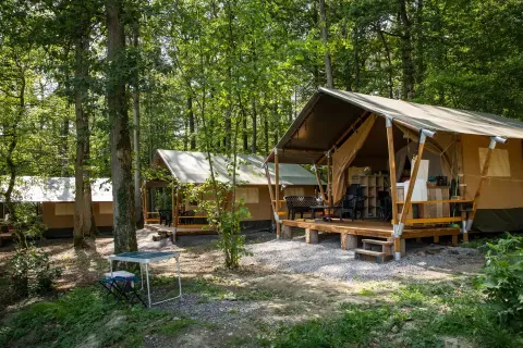 Tenda safari immersa nel bosco al Camping Le Roptai in Belgio, con veranda e arredi da esterno.