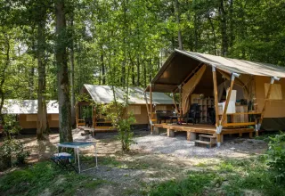 Tienda safari en el bosque en Camping Le Roptai, Bélgica, con terraza y muebles de exterior visibles.