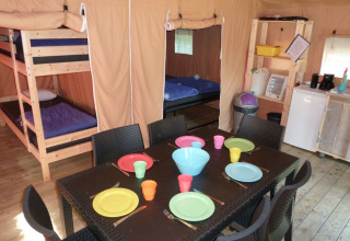 Interior de tienda safari con literas, mesa de comedor con platos de colores y zona de cocina equipada.