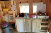 Pequeña cocina en una tienda safari con estufa, mini nevera, estantes, utensilios y papelera visible.