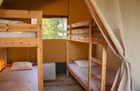 Interior de una tienda safari con dos literas de madera y ropa de cama, ideal para acampar en familia.