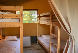 Interior de una tienda safari con dos literas de madera y ropa de cama, ideal para acampar en familia.