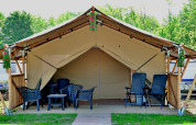 Outdoor safari tent with patio chairs and tables, floral decor, and greenery in the background.