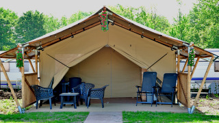 Tenda safari all'aperto con sedie, tavolino e decorazioni floreali, immersa nel verde e roulotte vicine.