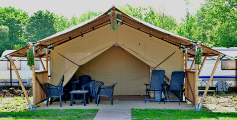 Safari tent met tuinmeubilair en bloemdecoratie, omgeven door groen en caravans op de achtergrond.