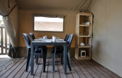 Eethoek in een safaritent met een zwarte tafel, zes stoelen en een houten kast vol servies.
