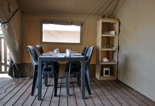 Ein Essbereich in einem Safarizelt mit schwarzem Tisch, sechs Stühlen und Regal mit Geschirr.
