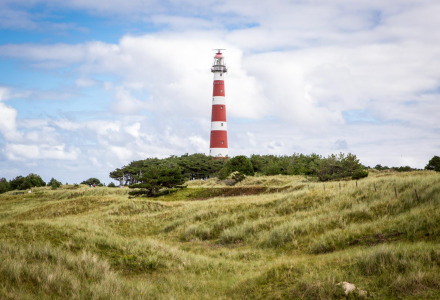 Faro rojo y blanco entre campos verdes cerca de Slappeterp, Friesland, Países Bajos, bajo un cielo parcialmente nublado.