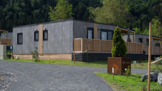 Moderne lodge ved Wulfenia Waterfront, Ossiacher See, Østrig, omgivet af grønne træer og bjerge.