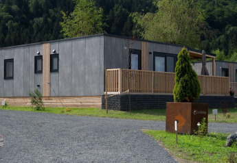 Moderne lodge ved Wulfenia Waterfront, Ossiacher See, Østrig, omgivet af grønne træer og bjerge.
