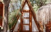 Cabaña de madera estilo A llamada Breña Tent en TAIGA Tarifa, España, rodeada de árboles y luz solar.