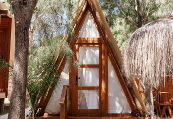 Cabane en bois en forme de A nommée Breña Tent à TAIGA Tarifa en Espagne, entourée d’arbres et de lumière.