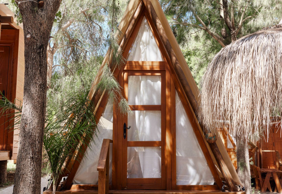 Cabane en bois en forme de A nommée Breña Tent à TAIGA Tarifa en Espagne, entourée d’arbres et de lumière.