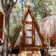 Cabaña de madera estilo A llamada Breña Tent en TAIGA Tarifa, España, rodeada de árboles y luz solar.