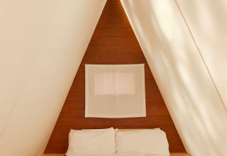 Vista interior de la Breña Tent en TAIGA Tarifa, España, con una cama acogedora en una habitación triangular.