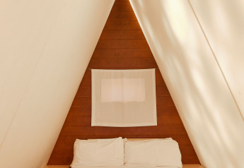 Vista interior de la Breña Tent en TAIGA Tarifa, España, con una cama acogedora en una habitación triangular.